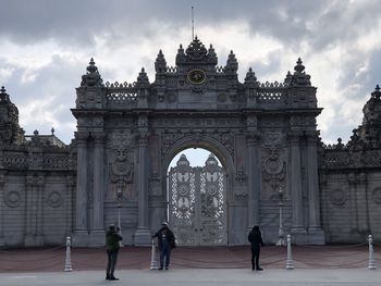 People walking in front of historical building against cloudy sky