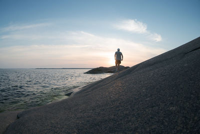A man walking along a rocky sea shore. back view
