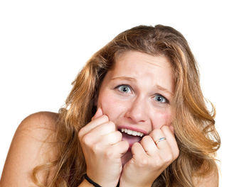 Close-up portrait of scared young woman with head in hands screaming against white background