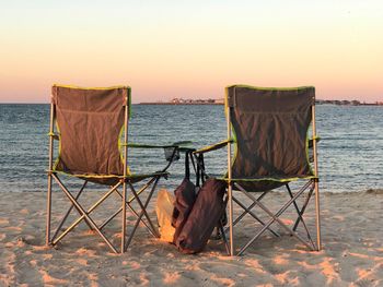 Deck chairs on beach against clear sky at sunset