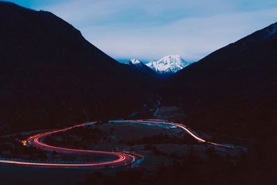 Light trails on road by mountains against sky at night