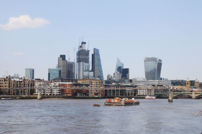 Modern buildings by river in city against sky