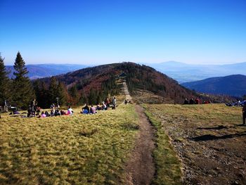 Group of people on landscape against clear blue sky