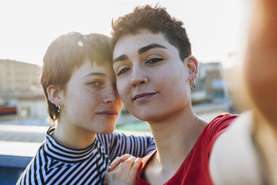 Close-up portrait of confident lesbian couple standing against clear sky in city