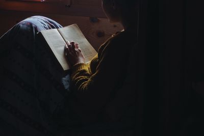 Young woman reading book in darkroom at home