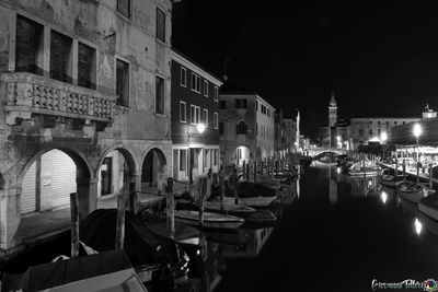 Boats moored in canal amidst buildings in city at night