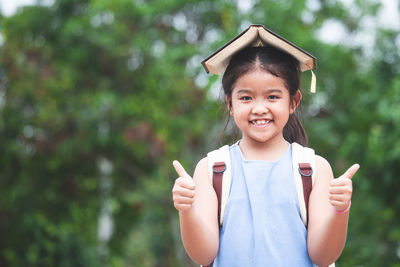 Portrait of smiling girl with book showing thumbs up