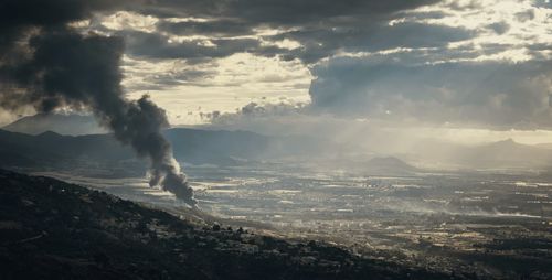 Smoke emitting from mountain against sky