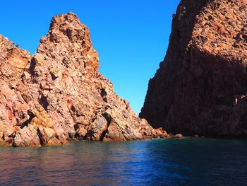 Rock formations by sea against clear blue sky