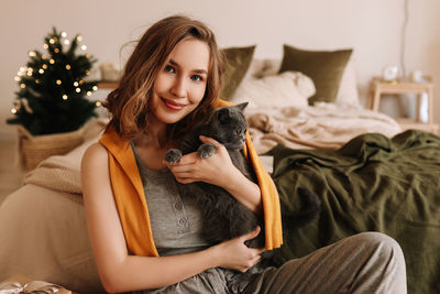 A pretty girl in pajamas rejoices and smiles during the christmas holidays in cozy bedroom interior