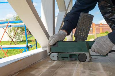 Carpenter smoothing wooden surface with belt sander outdoors