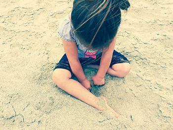 Low section of girl sitting on sand at beach