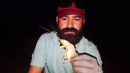 Low angle view of mid adult man holding giant grasshopper against sky at night