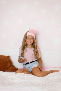 Girl is sitting on the bed in the pink bedroom, holding the phone in her hands and smiling