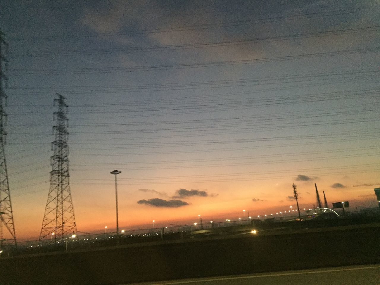 ELECTRICITY PYLONS ON FIELD AGAINST ORANGE SKY