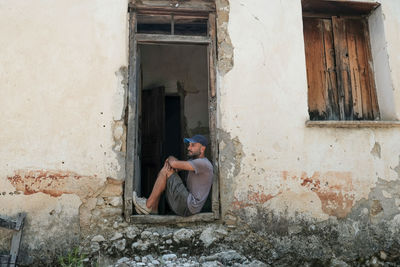 Side view of woman sitting on old abandoned house