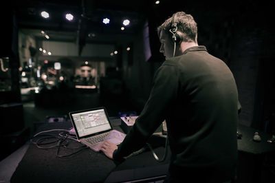 Rear view of man using laptop while standing in nightclub