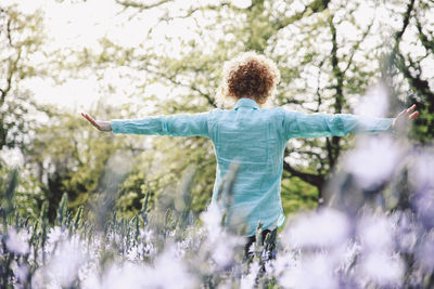 Woman standing with arms outstretched amidst flowering plants at forest