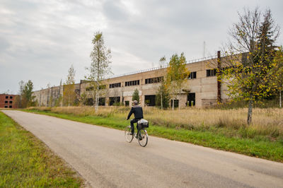 Man riding bicycle on road by building against sky