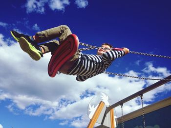 Low angle view of boy swinging against blue sky at playground