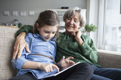 Grandmother and her granddaughter sitting together on the couch with digital tablet