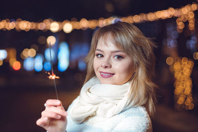 Portrait of smiling woman holding illuminated lighting equipment at night