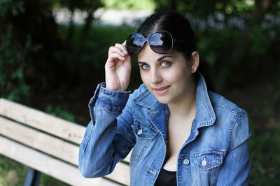 Portrait of beautiful young woman wearing sunglasses while sitting on bench
