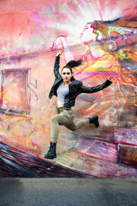 Portrait of woman jumping against graffiti wall