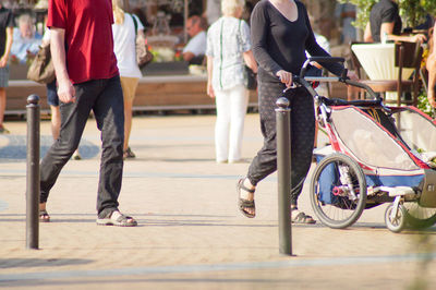 Low section of man walking by woman pushing baby carriage on footpath