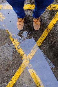 Low section of man standing by puddle on road with yellow marking