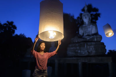 Low angle view of woman holding lit paper lantern at night