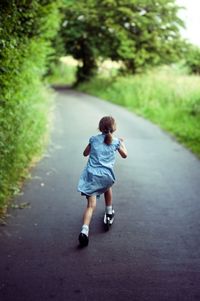 Rear view of girl on scooter  on road