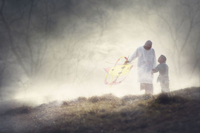 Grandfather and grandson holding kite while standing amidst fog