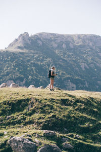 Full length of female hiker standing on field against mountain