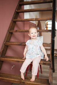 Cute smiling baby girl sits on wooden stair in modern appartment.