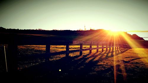 Fence on landscape against clear sky during sunset