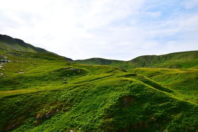 Scenic view of green hill against cloudy sky during sunny day