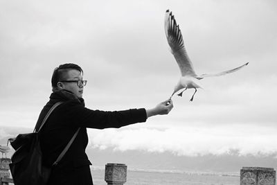 Man feeding seagull against clear sky