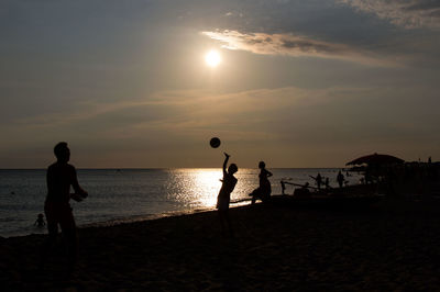 Silhouette people playing volleyball on beach against sky during sunset