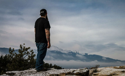 Rear view of man standing on mountain against sky