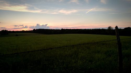 Scenic view of grassy field against sky at sunset