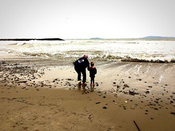 Rear view of friends walking on beach against clear sky