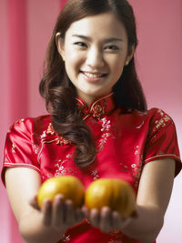 Portrait of smiling woman with oranges standing against backdrop