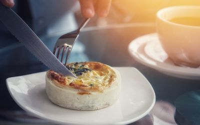 Close up woman hand is pressing knife on spanish cheese baked in tea time