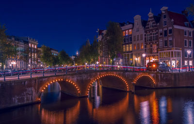 Bridge over canal amidst illuminated buildings in city at night