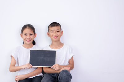 Portrait of siblings holding blackboard against white background