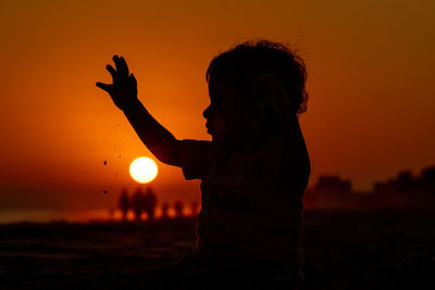 Silhouette baby playing at beach during sunset