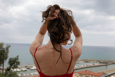 Rear view of young woman standing at sea against sky