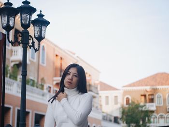 Portrait of young woman standing against buildings in city