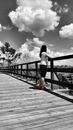 Rear view of woman standing on footbridge against sky